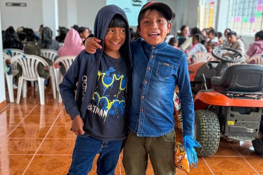 Two children stand together in front of a community gathering in Ecuador, where families and young people are seated for a Community Cinema event. A projection screen is visible in the background, and the activity provides a space for community participation, learning and shared experiences.