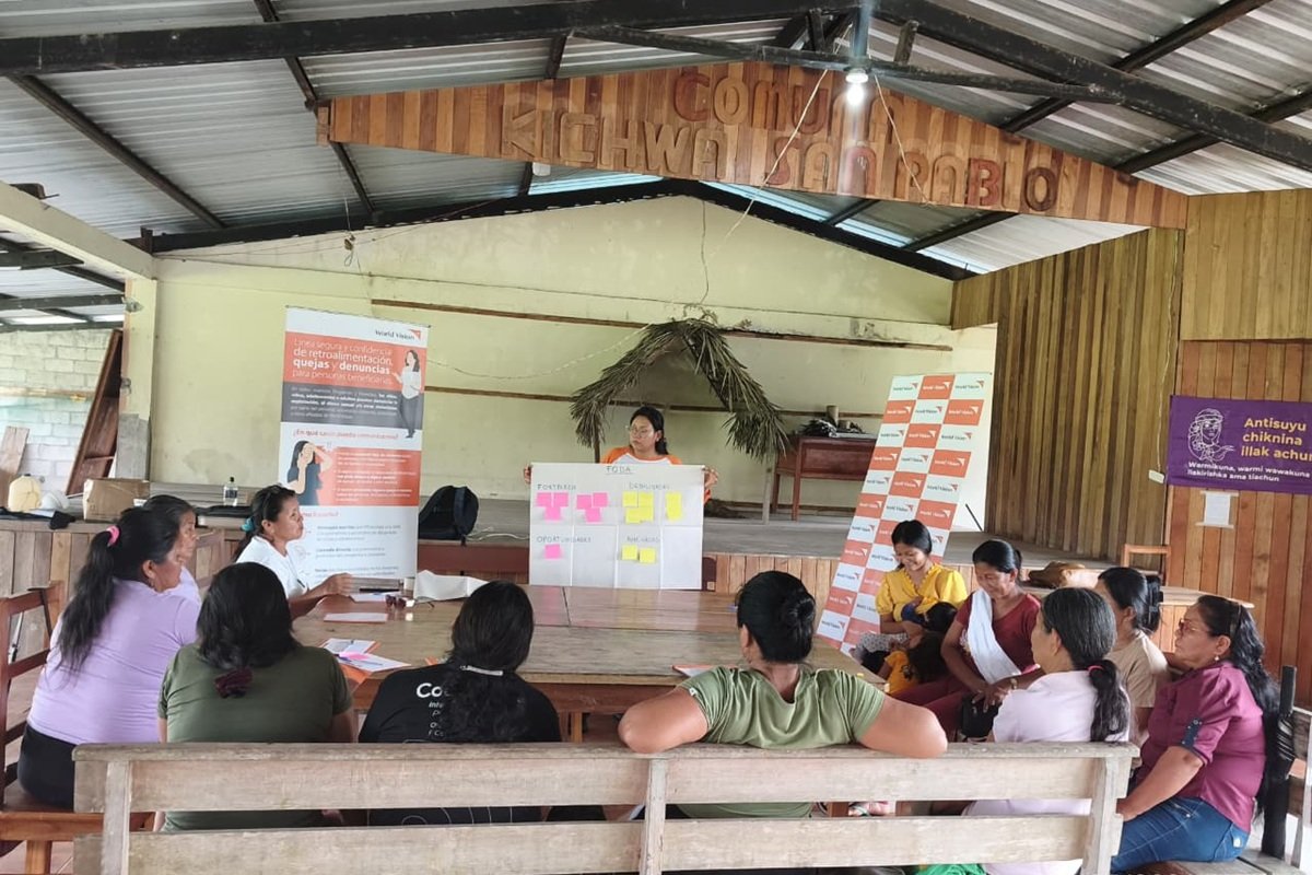 Participants sit together in a community meeting space in Ecuador while a facilitator presents a workshop exercise using a large board covered with notes. The display includes sections for strengths, opportunities and challenges as women from Sinchi Llanka Warmikuna share ideas and contribute to the discussion.