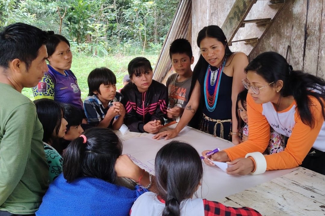 Young People and Communities Building Entrepreneurial Skills Through Shared Learning in Shakaim, Ecuador | Photo: World Vision | Image provided by World Vision Children, young people and adults gather around a large sheet of paper during a Business Model Workshop in the Shakaim Community, Ecuador. A facilitator records ideas while participants contribute to a group discussion in a rural forest setting. The activity forms part of the Youth Green project, which supports entrepreneurship, collaboration and sustainable community development.
