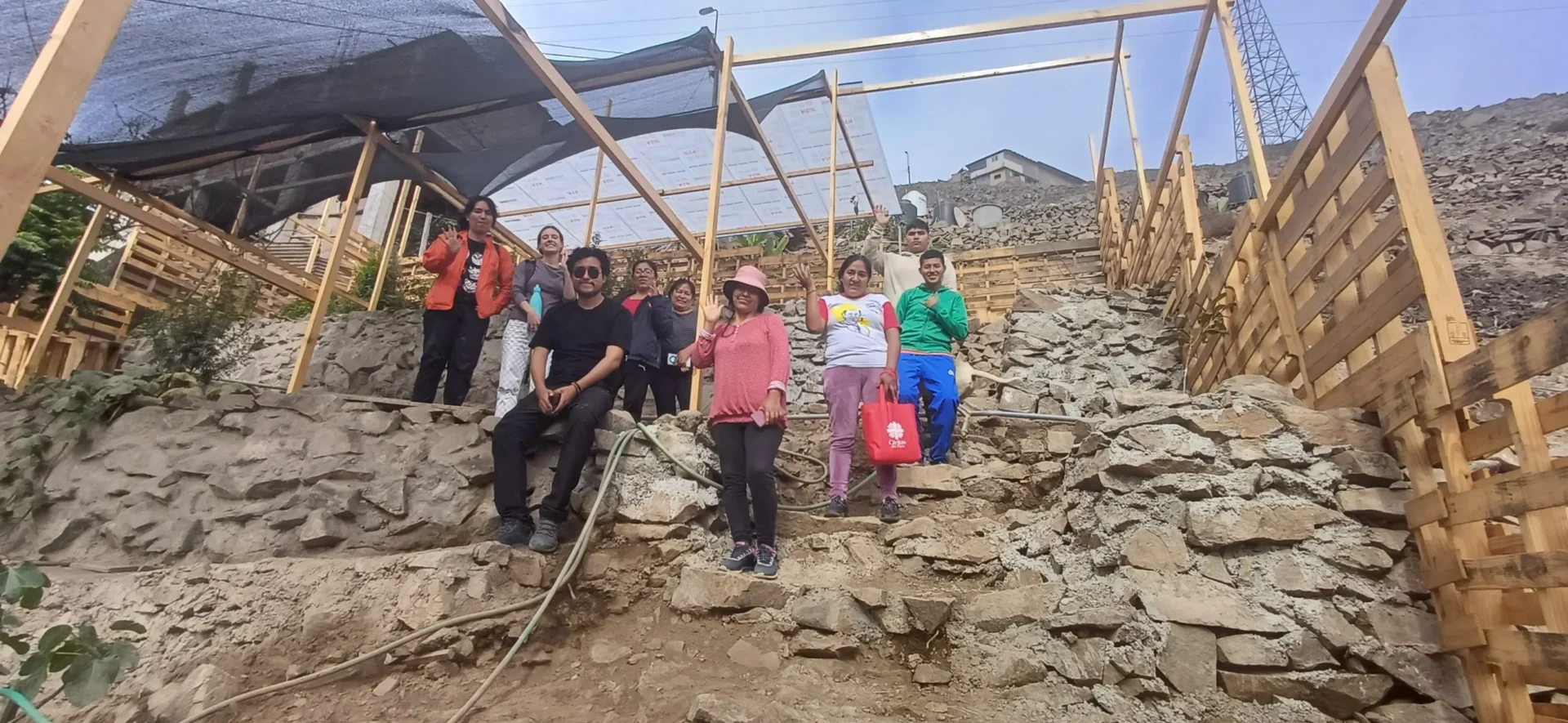 Communities and Schools Working Together to Build Urban Environmental Innovation in Lima, Peru | Photo: DESCO | Image provided by CAFOD Community members stand on a rocky hillside among wooden structures and terraced areas in Lima, Peru. The group gathers at a community site developed as part of an urban environmental initiative that promotes climate resilience, environmental awareness and safer living conditions in vulnerable neighbourhoods.
