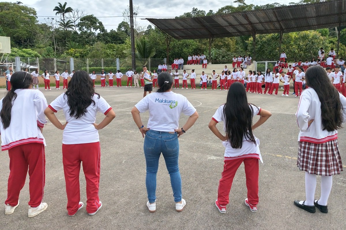 Students and Community Members Mark International Red Hand Day Through Dialogue and Collective Action in Colombia | Photo: Makikuna and War Child | Image provided by War Child Students stand in a large circle on a school sports court during a community dialogue session marking International Red Hand Day in Colombia. A facilitator stands in the centre while students and community members take part in activities held across the educational institution to encourage participation and discussion.