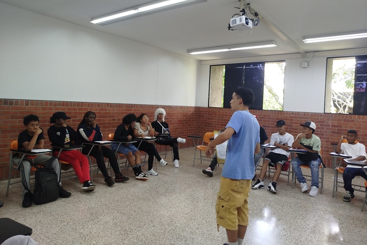 Participants in the Romper programme sit in a circle in a classroom at Universidad San Buenaventura in Colombia while one participant speaks during a simulated trial on environmental dilemmas. The activity encourages discussion and debate about environmental challenges and possible responses.