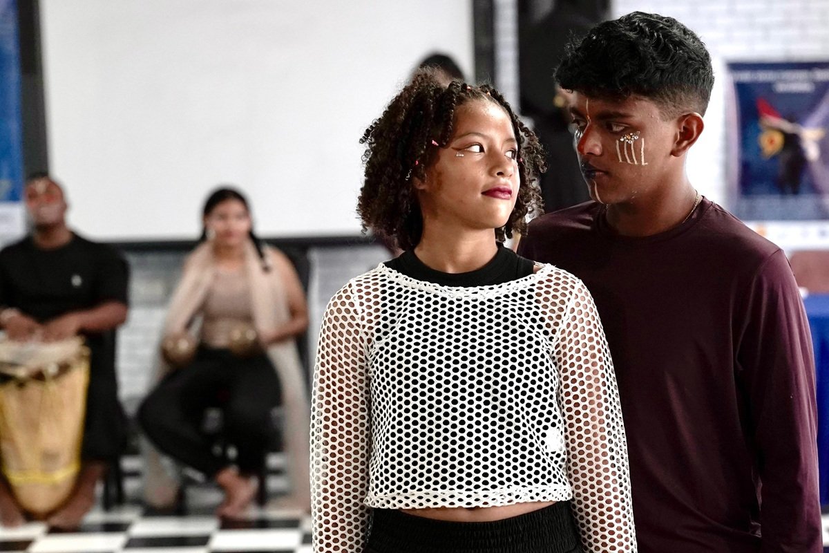 Two young participants perform a scene during a theatre activity in Barranquilla, Colombia. Face paint and costumes are used as part of a performance, while other participants and musicians are visible in the background. The activity forms part of a theatre project supported by Children Change Colombia to prevent sexual and gender-based violence.