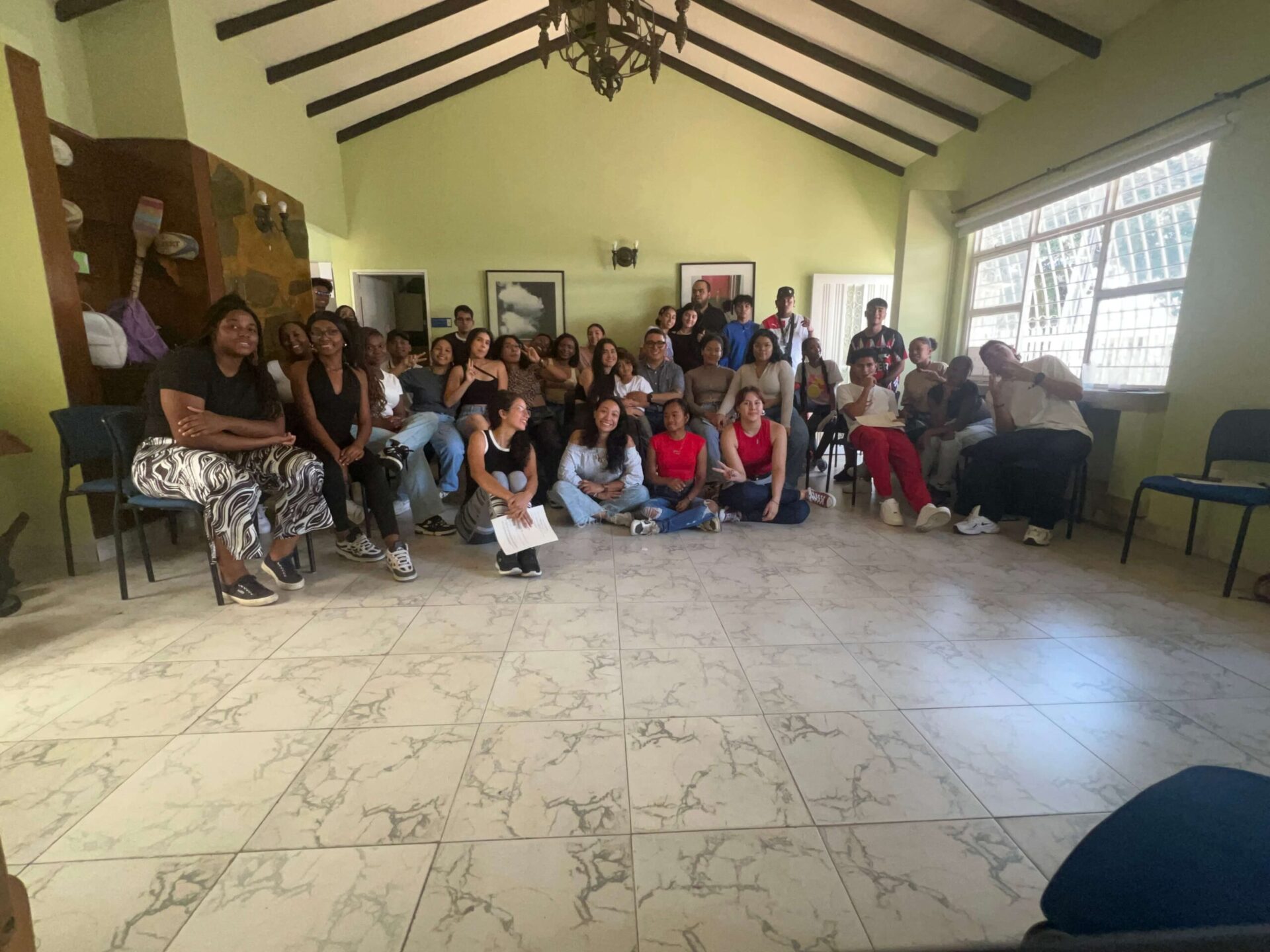 "Valientes" Group Reflect on Everyday Life and Wellbeing During a Group Gathering in Colombia | Photo: EMpower | Image provided by EMpower Participants in the “Valientes” programme gather in a community meeting room during a wellness session focused on the theme of Everyday Life. Young people sit and stand together in a large group, taking part in an activity designed to encourage reflection, discussion and connection with peers.